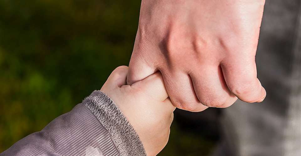 Das Foto zeigt einen Vater, der sein kleines Kind an der Hand hält. Dies verdeutlicht die gegenseitige Beziehung, die auf Liebe und Vertrauen basiert. Diese Beziehung bleibt bestehen, wenn beide sich weiterhin lieben.